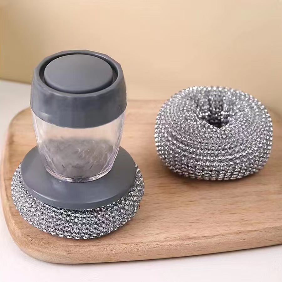 Soap dispenser steel brush with gray lid and base and metallic scrubber on a wooden board.