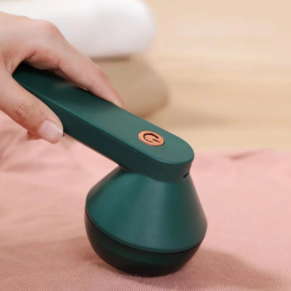 Green handheld electric lint remover with a button being held by a hand on a pink fabric.