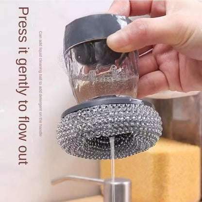 Hand holding a cleaning brush with liquid being dispensed from it, against a neutral background.