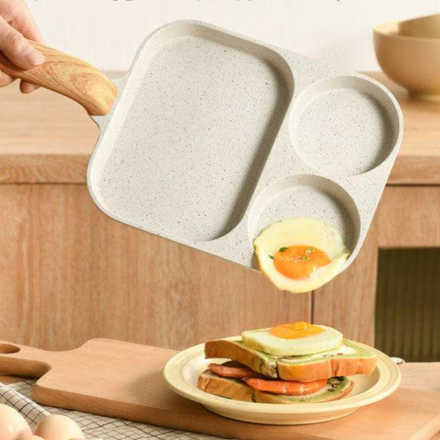 Person using a stone-look divided frying pan to cook eggs on a wooden table.