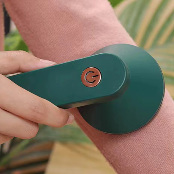 Person using a green electronic lint remover on their arm sleeve with a blurred natural background